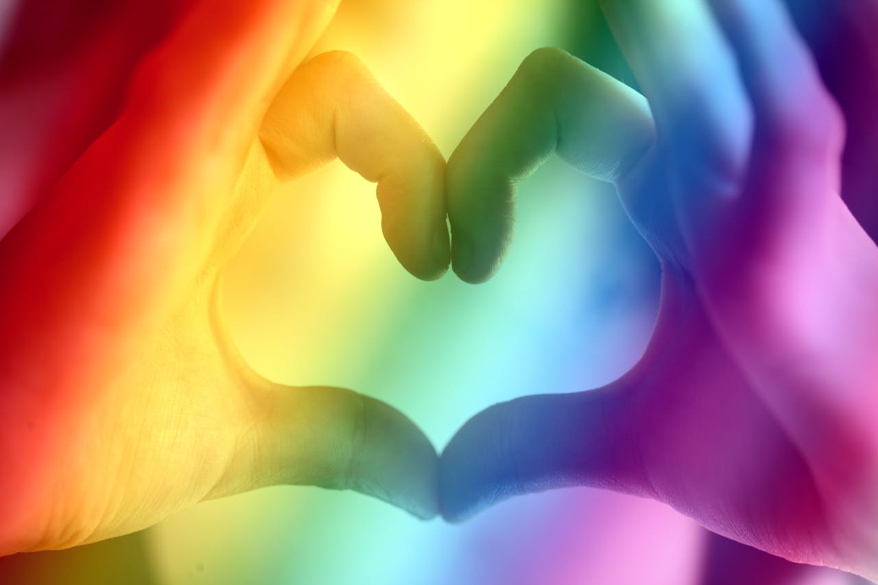 about-01 Hands forming a rainbow heart shape, symbolizing love, unity, and LGBTQ pride.