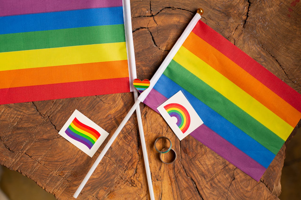 about-02 Overhead view of rainbow Pride flags and symbols on a wooden surface, signifying LGBTQ+ pride.